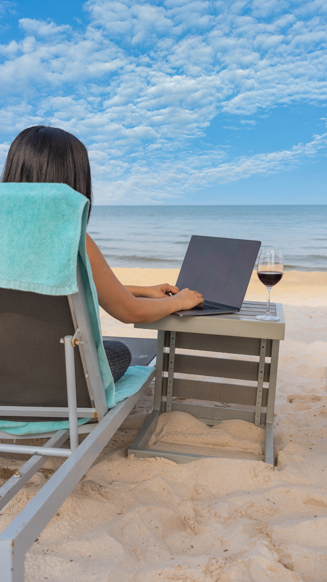 Frau sitzend auf einem Liegestuhl am Strand mit einem Laptop